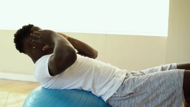 Jonge Afro-Amerikaanse man doet sit-up oefening met Swiss ball in de sportschool. Mannelijk fitness model dat een crunch in het fitnesscentrum uitvoert — Stockvideo