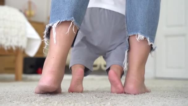 Donna scalza in jeans che insegna al bambino a camminare su un morbido tappeto bianco in un accogliente vivaio a casa — Video Stock