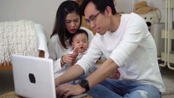 Asiatisk far arbetar med bärbar dator med sin fru och söt asiatisk pojke när du sitter på golvet i mysiga rum hemma — Stockvideo