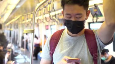 Yeni Coronavirus Covid-19 zatürree salgını sırasında siyah cerrahi maske takan ve metroda cep telefonu kullanan genç bir Asyalı 'ya yaklaş.