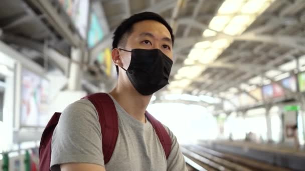 Blisko jeden młody Azjata w czarnej chirurgicznej masce twarzy czeka na pociąg podczas nowego typu Coronavirus Covid-19 ogniska zapalenia płuc i pm 2,5 kryzys zanieczyszczenia powietrza smogu w dużym mieście — Wideo stockowe