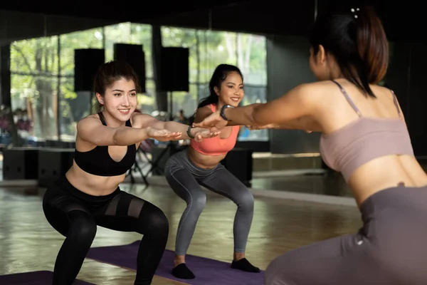 Gruppe glücklicher asiatischer Frauen, die im Aerobic-Kurs Kniebeuge-Übungen auf Yogamatten machen. Junge Sportler lächeln beim Training im Fitnessstudio. — Stockfoto