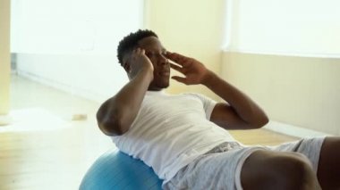 Genç Afro-Amerikan adam spor salonunda İsviçre topu ile sit-up egzersiz yapıyor. Erkek fitness modeli fitness merkezinde bir crunch performans