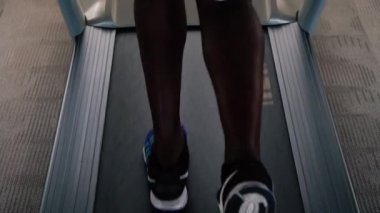 Mavi spor ayakkabılı Afrikalı Amerikalı sporcu fitness kulübünde elektrikli koşu bandında çalışıyor. Koşu bandında koşan yüzü olmayan erkek koşucu.