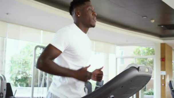 Aşağıdan uygun Afro-Amerikan adam gündüz spor salonunda elektrikli koşu bandı üzerinde çalışan. Sporcu antrenman makinesi üzerinde çalışıyor — Stok video
