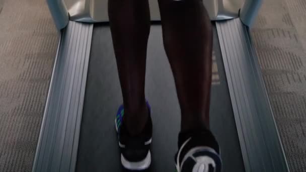 African American Idrottsman i blå sneakers tränar på elektriska löpband i fitness club. Ansiktslös löpare på löpband — Stockvideo