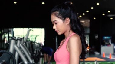 Gülümseyen ve kararlı Asyalı genç bayan sporcu kollarını kavuşturup spor salonunda dururken kameraya bakıyor.