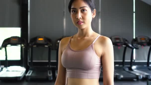 Sonriente y determinada joven atleta asiática mirando a la cámara mientras pone los brazos cruzados y de pie en el gimnasio gimnasio — Vídeos de Stock