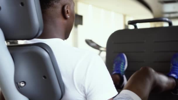 Visszapillantás afro-amerikai férfi gyakorolja a láb sajtó alatt fitness edzés a modern tornaterem — Stock videók