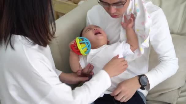 Young Asian father sitting on floor and holding infant boy while mother holding baby clothing and together taking care of son and changing diapers — Stockvideo