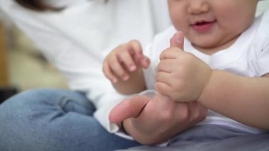 Asyalı bebek evde dinlenirken annesinin elini tutuyor.
