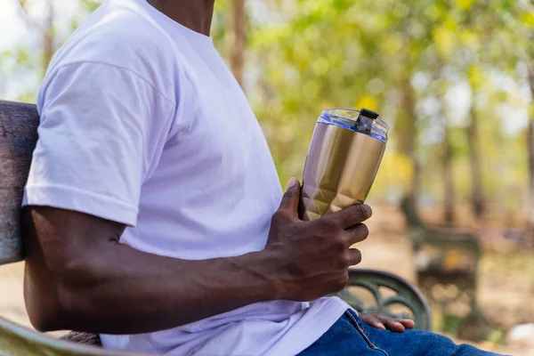 Close-up of young adult African American holding an insulated bottle mug sitting in the park - with copy space — Stockfoto