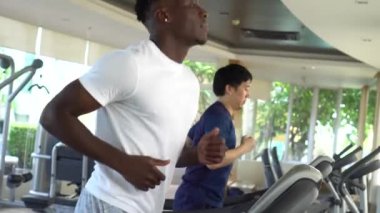 Spor salonundaki koşu bandında çalışan çok ırklı sporcular. Koşu bantlarında koşan çok ırklı Asyalı ve Afrikalı Amerikalı erkekler