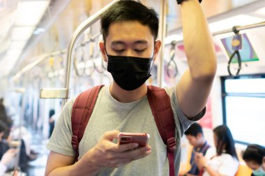Yeni Coronavirus Covid-19 zatürree salgını sırasında siyah cerrahi maske takan ve metroda cep telefonu kullanan genç bir Asyalı 'ya yaklaş.