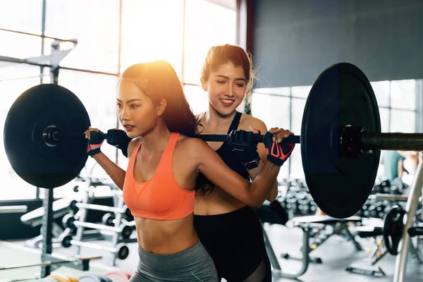 Asyalı kişisel antrenör vücut geliştiren bir kadına spor salonunda halterle egzersiz yapması için koçluk yapıyor.. — Stok fotoğraf