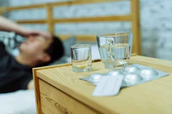 Giovane uomo asiatico si sente male e malato sdraiato sul letto con farmaci compresse e pillole sul tavolo — Foto Stock