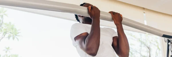 Forte sportivo afroamericano in t-shirt bianca che fa pull up durante l'allenamento di fitness in palestra moderna — Foto Stock