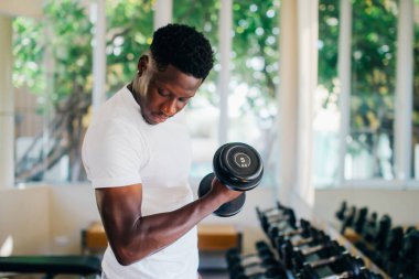 Genç Afrikalı Amerikalı adam spor salonundaki halterleri kaldırıyor ve ayakta duruyor.