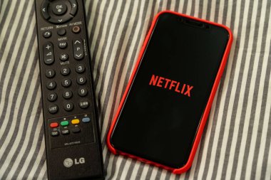 BANGKOK, THAILAND - 27 Mart 2020: yatakta oturan adam Netflix logosunu akıllı telefon ekranında tutuyor. Netflix internet üzerinden yayın yapan bir eğlence şirketidir.