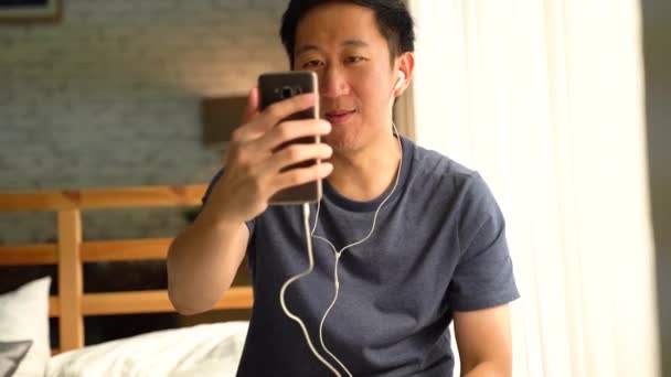 Ritratto di felice uomo asiatico di 30 anni in abbigliamento casual che fa videochiamate facetime con smartphone a casa. Sta salutando la gente sullo schermo del telefono . — Video Stock