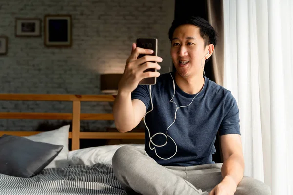 평범 한 옷을 입고 있는 30 대의 행복 한 동양인의 모습 집에서 스마트폰으로 전화하는 실시간 비디오를 찍고 있다. 전화 화면에 사람들에게 손을 흔들며. — 스톡 사진