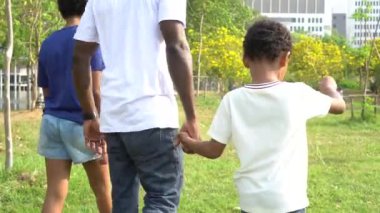 African American father walking in the nature with pre-teen daughter and holding hands with son. Recreational family gathering on weekend