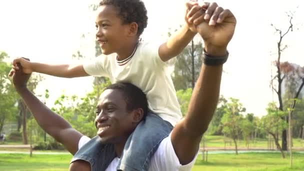 屋外公園で幸せなアフリカ系アメリカ人の父と息子のピギーバック。家族の週末活動 — ストック動画