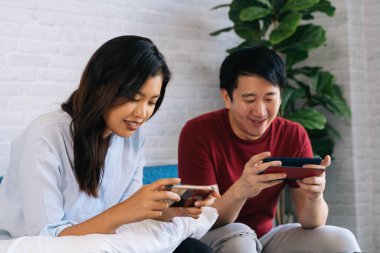 Genç erkek ve bayan arkadaşlar evde cep telefonuyla oyun oynuyorlar. Asyalı erkek ve kadın bilgisayar oyunu oynamak için akıllı telefon kullanıyor.