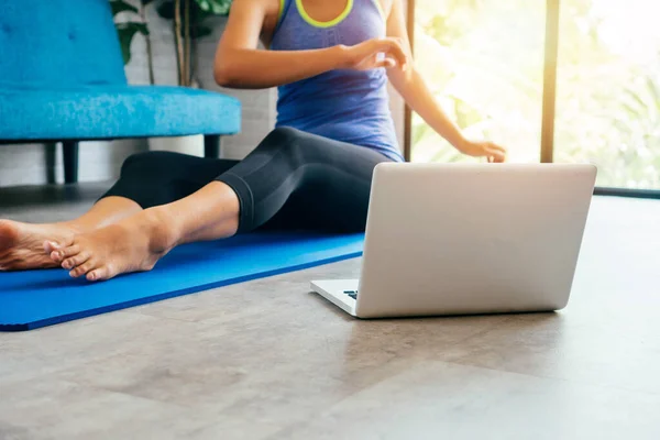 20s young Asian woman in sportswear doing sterching exercises while watching yoga training class on computer laptop online. Healthy girl exercising in living room with sofa couch in the background — Stock Photo, Image