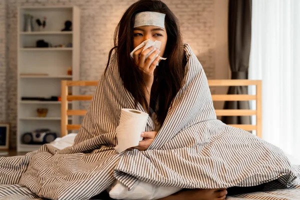 Genç Asyalı kadın soğuk ve hastalıktan muzdarip ve evinde dokularla yatakta yatıyor. — Stok fotoğraf