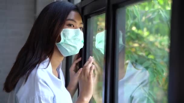 Wanita sakit dari karantina coronavirus melihat melalui jendela dan mengenakan topeng untuk perlindungan saat pulih dari penyakit pandemi virus korona di rumah. Pasien terisolasi untuk mencegah infeksi — Stok Video