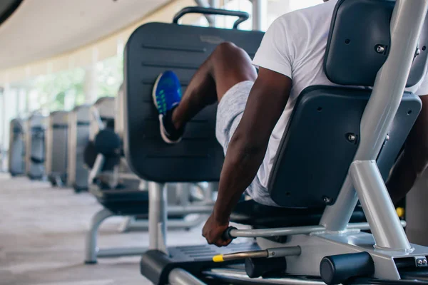 Вид на афроамериканца, делающего упражнения на прессе для ног во время фитнес-тренировок в современном тренажерном зале — стоковое фото