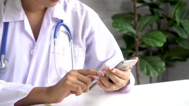 Νεαρή Ασιάτισσα γιατρός χρησιμοποιεί κινητό στο νοσοκομείο. Μηνύματα κειμένου κύλισης και δακτυλογράφησης εργαζομένων υγειονομικής περίθαλψης στο γραφείο — Αρχείο Βίντεο