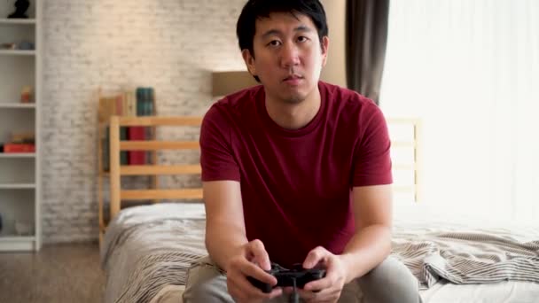 Jeune homme tenant contrôleur de jeu tout en jouant à un jeu vidéo console. Asiatique gars en utilisant manette de jeu à la maison . — Video