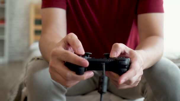 Primer plano del joven que sostiene el controlador de juego mientras juega videoconsola. asiático chico usando gamepad joystick en casa — Vídeo de stock