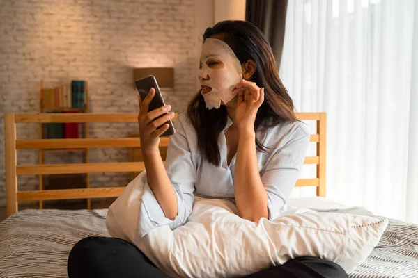아시아인 소녀 가 침실에서 컴퓨터 랩탑을 사용하는 동안 얼굴에 마스크를 쓰는 모습. 여성의아름다움 과 인종간의 돌봄 개념 — 스톡 사진