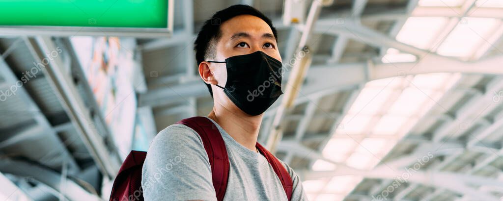 Close up of one young Asian man wearing a black surgical face mask waiting for the train during new type Coronavirus Covid-19 pneumonia outbreak and pm 2.5 smog air pollution crisis in big city