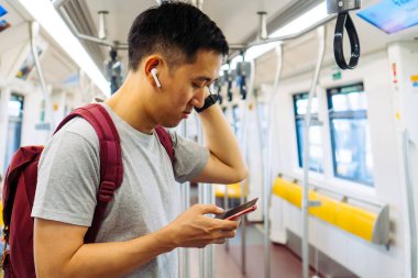 Genç adamın kablosuz kulaklıklarla müzik dinlemesini ve trenle gidip gelirken cep telefonu kullanmasını kapatın. Asyalı adam müzik dinlemekten hoşlanıyor.