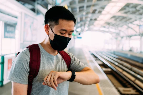 Close up de um jovem asiático vestindo uma máscara facial cirúrgica preta esperando o trem durante o novo tipo Coronavirus Covid-19 surto de pneumonia e pm 2,5 smog crise de poluição do ar na cidade grande — Fotografia de Stock