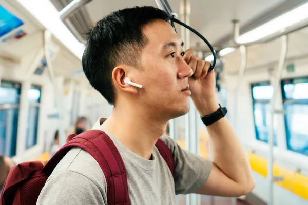 Close up de jovem ouvindo música com fones de ouvido sem fio enquanto viaja de trem. Asiático cara gostando de música em movimento — Fotografia de Stock