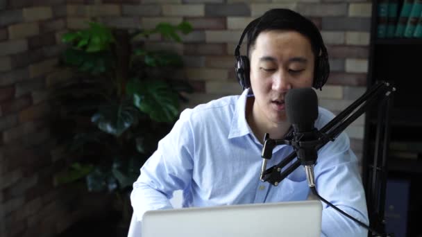 Young adult businessman podcasting and recording talk show at home studio with computer laptop on table. The desk is attached with microphone. Podcast and home audio recording concept — Stock Video