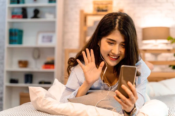 Retrato de feliz 20s mulher asiática envelhecida em roupas casuais fazendo videochamada em tempo real com smartphone em casa. Ela acena para as pessoas na tela do telefone . — Fotografia de Stock