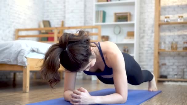 Sterk fitness meisje in atletische sportkleding doet een plank workout. Aziatische vrouw training thuis in haar woonkamer met gezellige sofa home interieur setting — Stockvideo