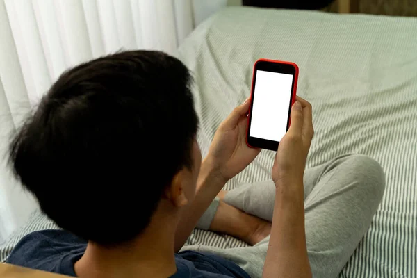Незапоминающийся мужчина держит на руках смартфон с пустым местом на экране для любого текстового сообщения. Удобно расположившись на кровати в спальне . — стоковое фото