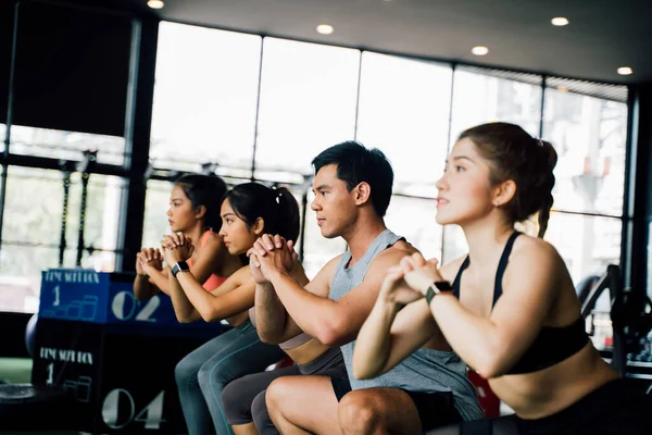 Gruppe athletischer junger asiatischer Menschen in Sportbekleidung beim Kniebeugen und Turnen in der Turnhalle. — Stockfoto