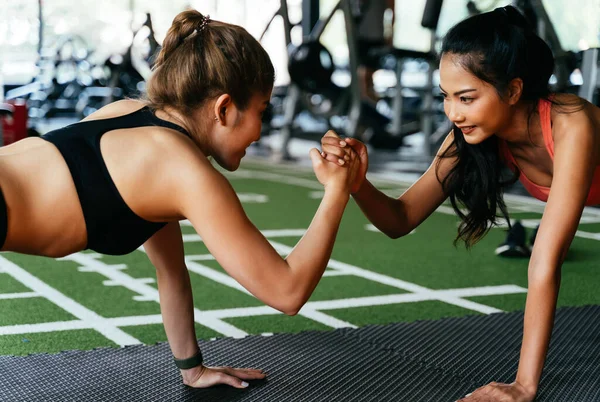 Gesund lächelnde Freundinnen, die sich gegenseitig hoch fünf geben, während sie sich im Fitnessstudio nach oben schieben. Asiatische Sportler trainieren gemeinsam. — Stockfoto