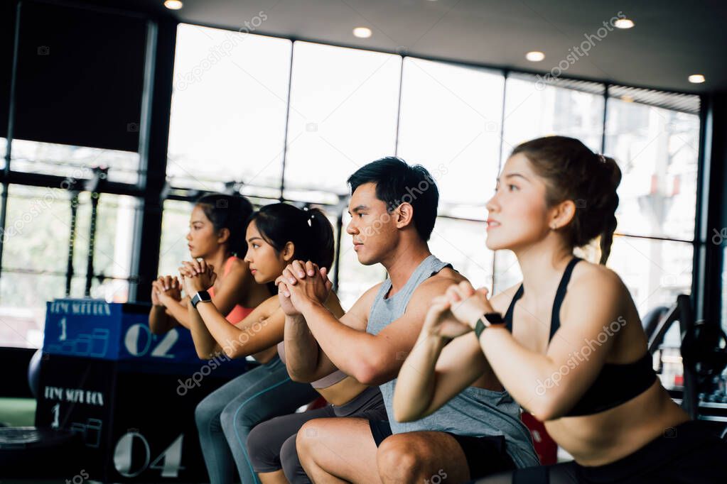 Group of athletic young Asian people in sportswear doing squat and exercising at the gym.