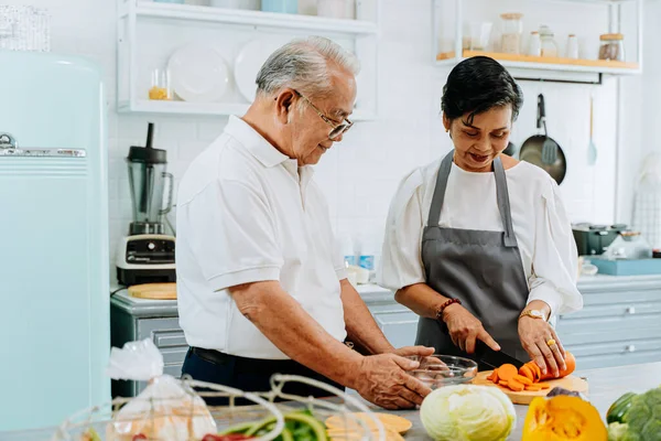 Starsza Azjatka gotuje jedzenie w kuchni. Osoby w podeszłym wieku lat 70-tych mężczyzna i kobieta przygotowują składniki w kuchni licznik razem — Zdjęcie stockowe