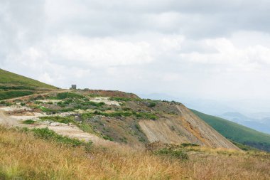 Uzak küçük avcı kulübesi çimenli, yüksek dağ yamacına bakan bulutlu gökyüzüne karşı
