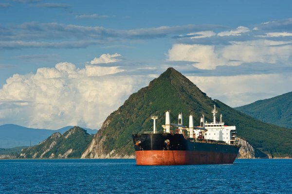 На заднем плане горного побережья стоит большой навалочный транспортник.
.